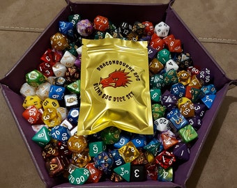 May include: A purple velvet dice tray filled with a variety of colorful dice. A gold pouch with the text "Dragonbourne RPG Blind Bag Dice Set" is in the center of the tray.