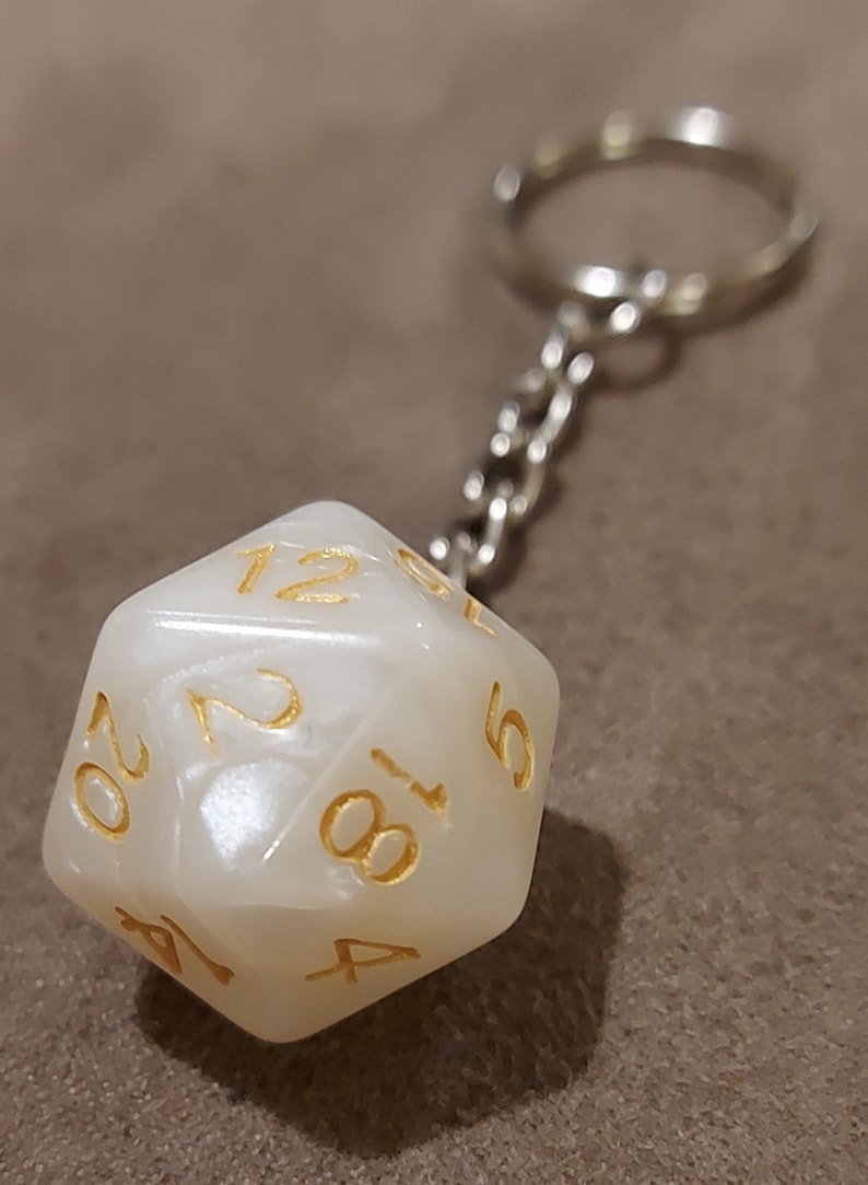 May include: A white, iridescent, 20-sided dice keychain with gold numbers. The keychain is attached to a silver metal chain.