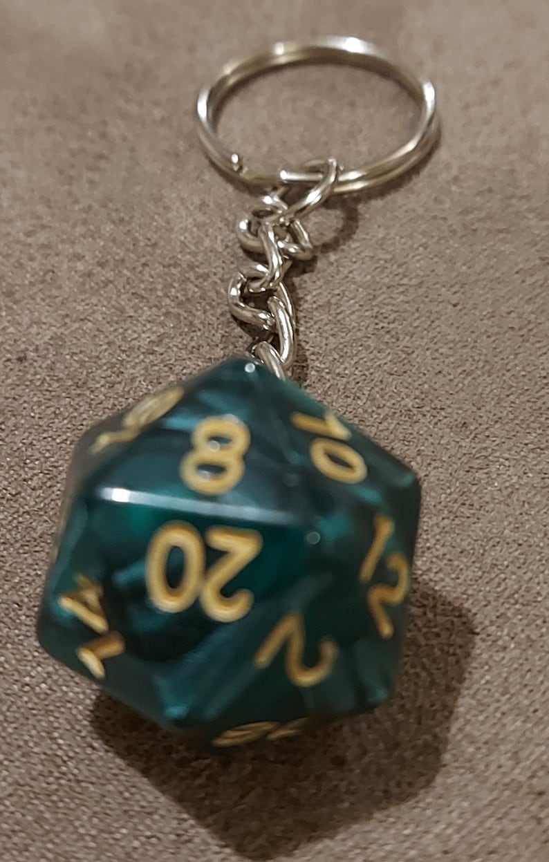 May include: A teal green 20-sided die keychain with gold numbers. The die is attached to a silver keychain.