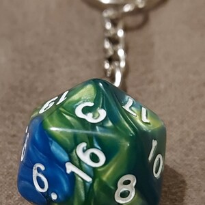 May include: A green, blue, and gold iridescent keychain with a 10-sided die. The die has white numbers on each side.