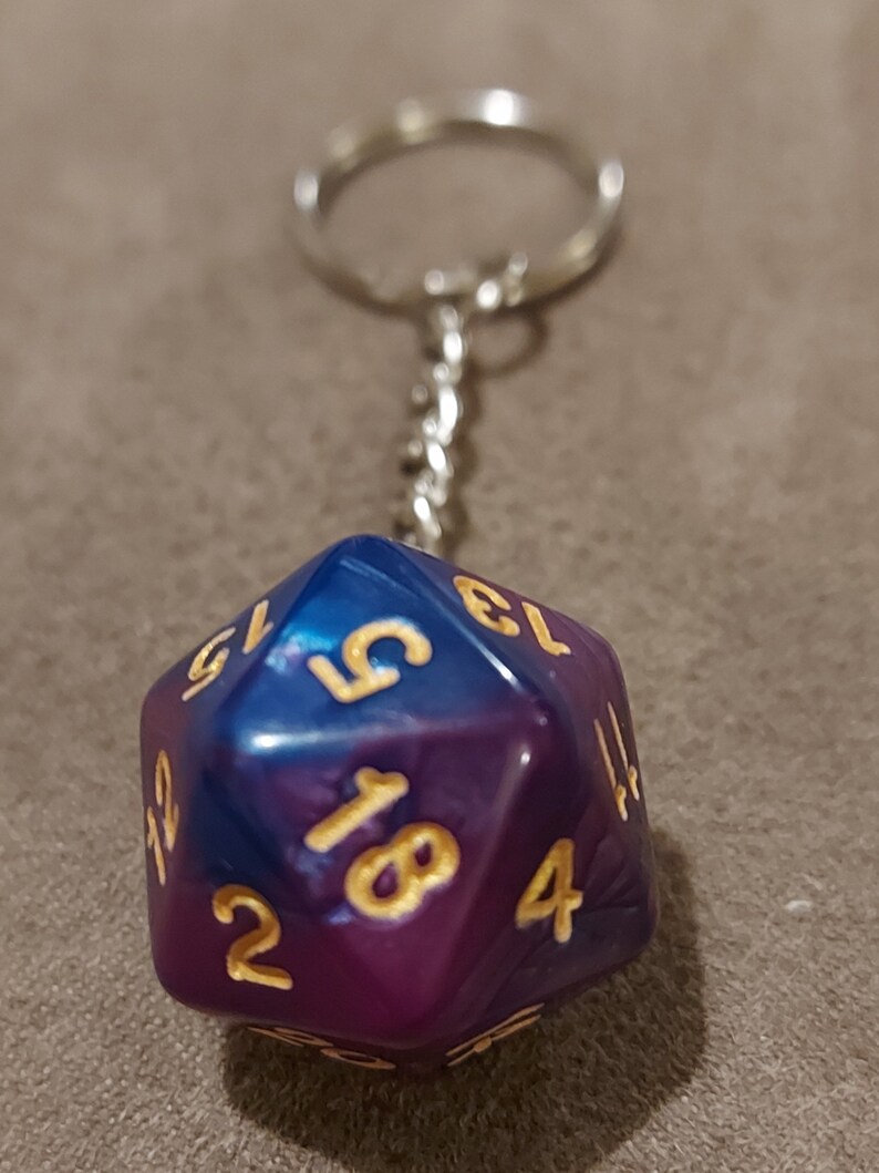 May include: A purple and blue iridescent d20 dice keychain with gold numbers. The keychain is attached to a silver metal ring.