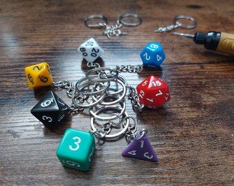 May include: A set of six colorful dice keychains, each with a different number, attached to a silver chain with multiple key rings. The dice are red, blue, yellow, black, green, and purple.