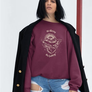 May include: A maroon sweatshirt with a graphic design of a sun, moon, and whale with the text "as above so below".