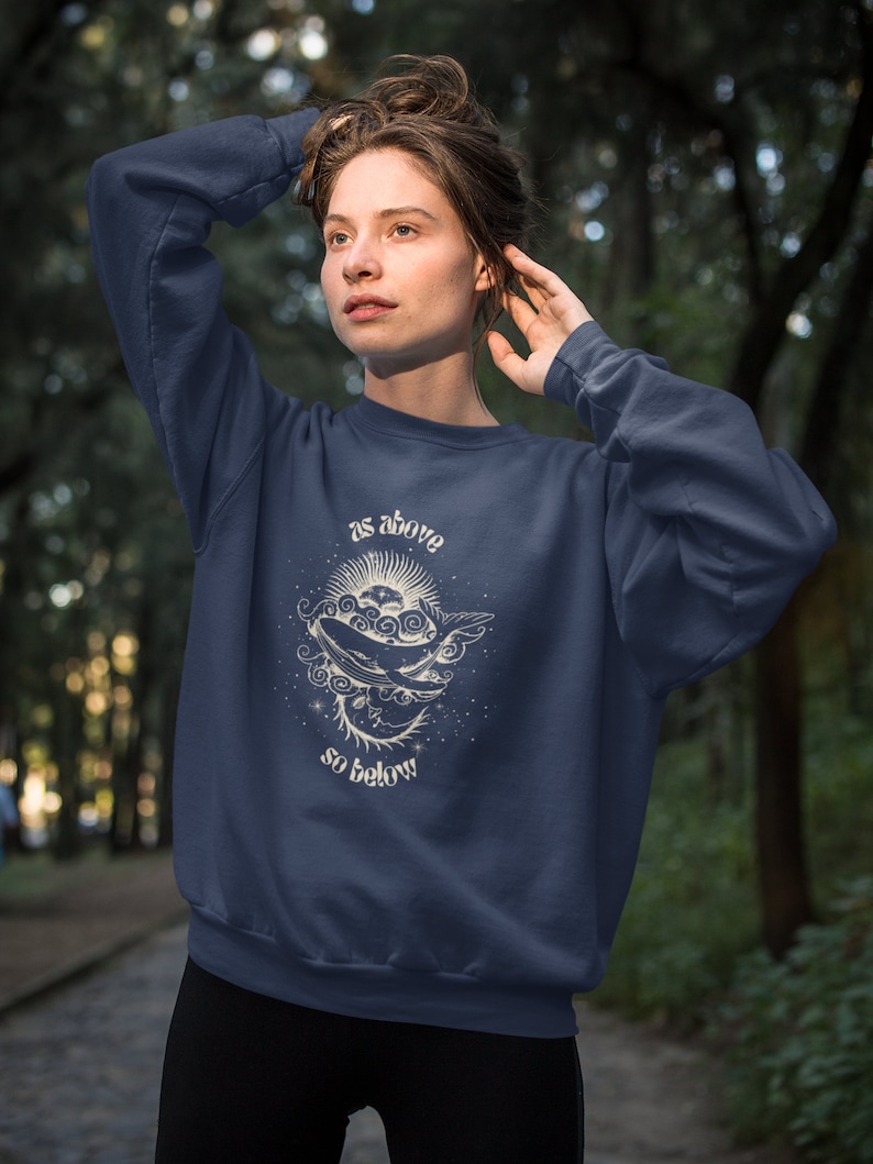 May include: A navy blue sweatshirt with a white graphic of a whale swimming in a starry sky. The graphic includes the text "as above so below".