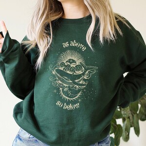 May include: A dark green sweatshirt with a graphic print of a whale in a crescent moon with the text "as above so below".