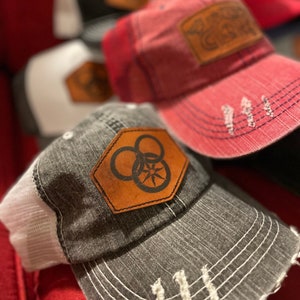 May include: A stack of five different colored baseball caps with various embroidered patches. The patches include a biohazard symbol, a compass, and a logo with the text "Dirt Road Gypsy".