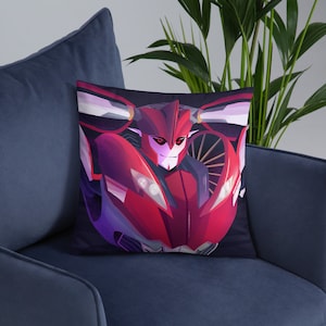 May include: A red and black pillow featuring a robot character with a menacing expression. The robot has a red body with black accents and a black face with red eyes. The pillow is a great addition to any Transformers fan's home.