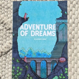 Puede incluir: Portada de libro con el título "ADVENTURE OF DREAMS" en blanco. La ilustración presenta un paisaje de fantasía con cielo azul, acantilados oscuros, un puente y criaturas caprichosas. El subtítulo dice "AN ILLUSTRATED JOURNEY."