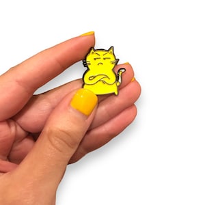 Può includere: Spilla in smalto giallo di un gatto dei cartoni animati con le braccia incrociate e un'espressione scontrosa.
