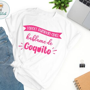 May include: White t-shirt with pink text that reads "Forget pumpkin spice, hablame de Coquito".