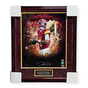 May include: Framed image of Jayden Daniels, Washington Commanders quarterback, holding a football. The background features a fiery design with the text "AP NFL OFFENSIVE ROOKIE OF THE YEAR." The frame is dark wood with a gold border.