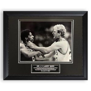 May include: Framed black and white photograph featuring basketball players Dr. J and Larry Bird in a moment of confrontation. The photograph is matted and framed in a black frame with a beaded edge. A plaque at the bottom identifies the players and the date.