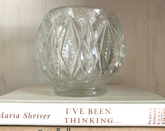 Könnte beinhalten: Eine klare Glasschale mit einem gepressten Rauten- und Sternmuster. Die Schale hat eine abgerundete, bauchige Form mit einem kleinen kreisförmigen Boden. Das Glas ist transparent und reflektiert das Licht, was die geometrischen Texturen betont.