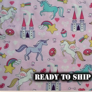 May include: Pink fabric with a repeating pattern of unicorns, castles, rainbows, stars, donuts, cupcakes, and hearts. The text "READY TO SHIP" is printed on the fabric.