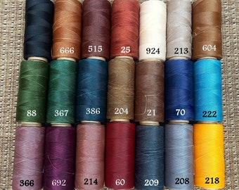 Puede incluir: Una colección de 18 carretes de hilo encerado en varios colores, incluyendo negro, marrón, rojo, blanco, verde, azul, morado y amarillo. Cada carrete está etiquetado con un número.