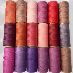 Può includere: Una collezione di 16 bobine di filo da ricamo in varie tonalità di rosa, rosso, viola e arancio.