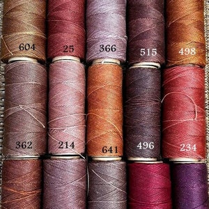 Peut inclure: Dix bobines de fil de différentes nuances de brun, rouge et violet. Les bobines sont numérotées : 604, 25, 366, 515, 498, 362, 214, 641, 496, 234, 631, 567, 362, 60 et 632.