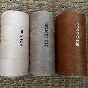May include: Three spools of thread in different colors: white, light brown, and brown. The spools are labeled with numbers and names: 924 Sand, 213 Eisbraun, and 604 Old Gold.