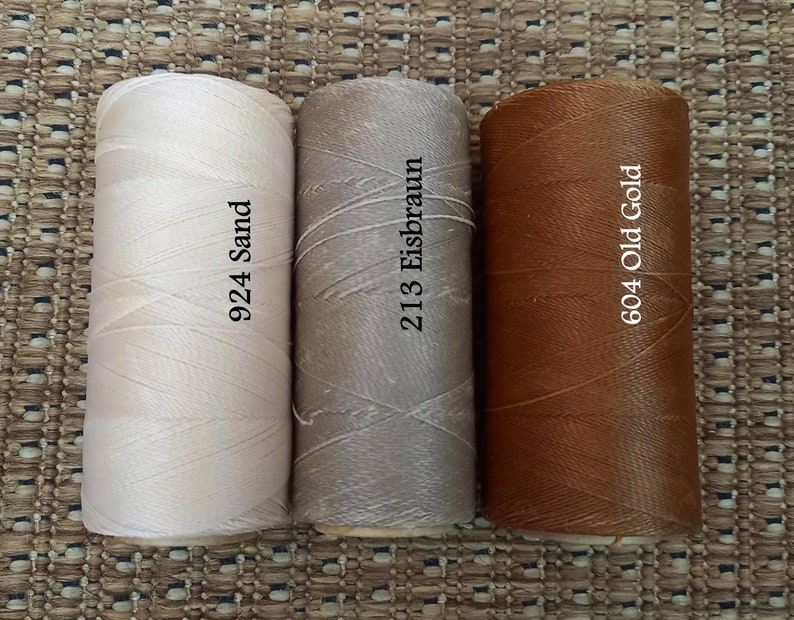 May include: Three spools of thread in different colors: white, light brown, and brown. The spools are labeled with numbers and names: 924 Sand, 213 Eisbraun, and 604 Old Gold.