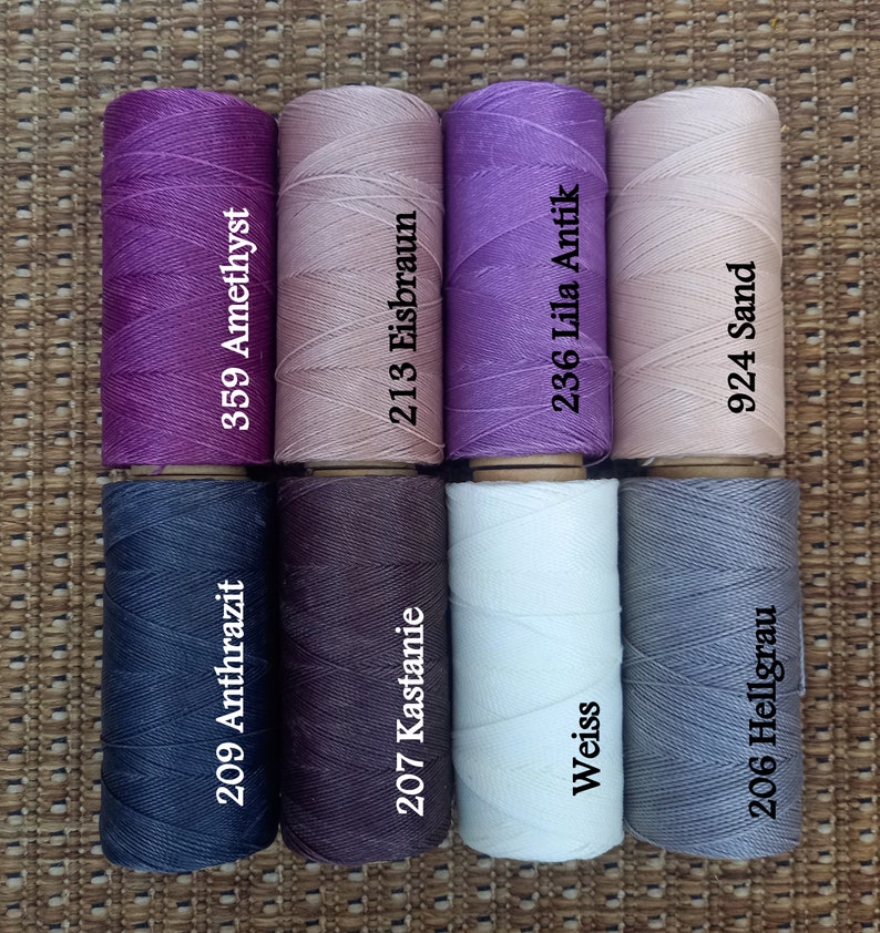 Pode incluir: Oito carret&eacute;is de fio em v&aacute;rias cores, incluindo roxo, rosa, marrom, branco e cinza. Cada carretel tem um n&uacute;mero e um nome de cor impresso. Os n&uacute;meros s&atilde;o 209, 359, 207, 213, 236, 924, 206, e os nomes das cores s&atilde;o Anthrazit, Amethyst, Kastanie, Eisbraun, Lila Antik, Sand e Hellgrau.