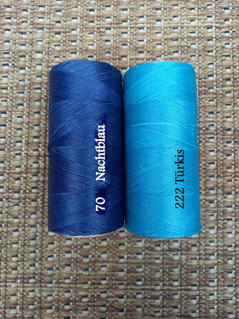 May include: Two spools of thread, one dark blue and one turquoise. The dark blue spool has the text "70 Nachtblau" printed on it. The turquoise spool has the text "222 T&uuml;rkis" printed on it.