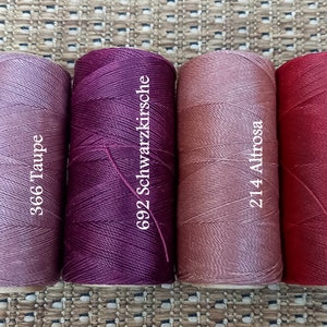 May include: Four spools of thread in different shades of pink, red, and purple. The spools are labeled with numbers and names: 366 Taupe, 692 Schwarzkirsche, 214 Altrose, and 60 Weinrot.