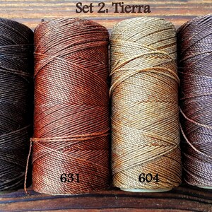 Puede incluir: Conjunto de cuatro carretes de hilo de lino encerado en tonos marrones, naranja, beige y marr&oacute;n oscuro. Los carretes est&aacute;n etiquetados con los n&uacute;meros 496, 631, 604 y 515. El texto "Set 2: Tierra" se muestra encima de los carretes.