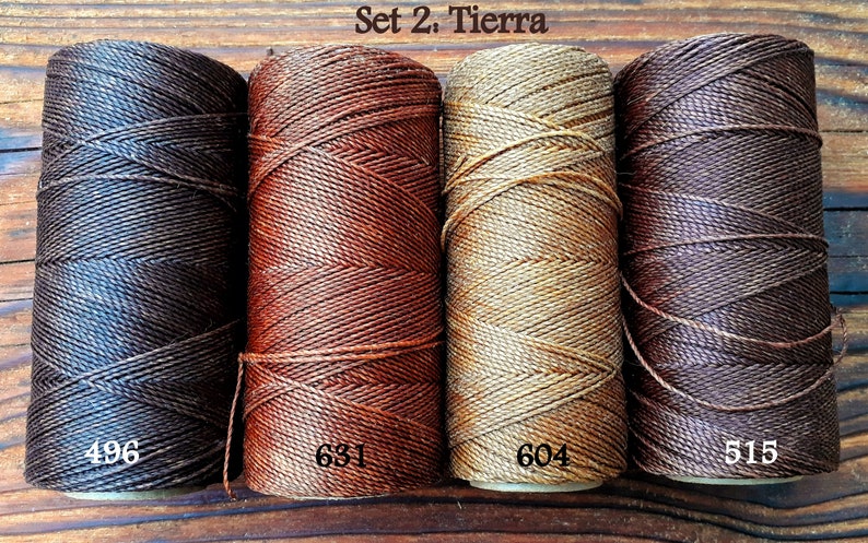 Puede incluir: Conjunto de cuatro carretes de hilo de lino encerado en tonos marrones, naranja, beige y marr&oacute;n oscuro. Los carretes est&aacute;n etiquetados con los n&uacute;meros 496, 631, 604 y 515. El texto "Set 2: Tierra" se muestra encima de los carretes.