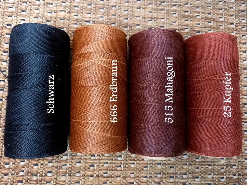 May include: Four spools of waxed thread in different colors: black, brown, burgundy, and copper. The spools are labeled with the color names and numbers: "Schwarz", "666 Erdbraun", "515 Mahagoni", and "25 Kupfer".