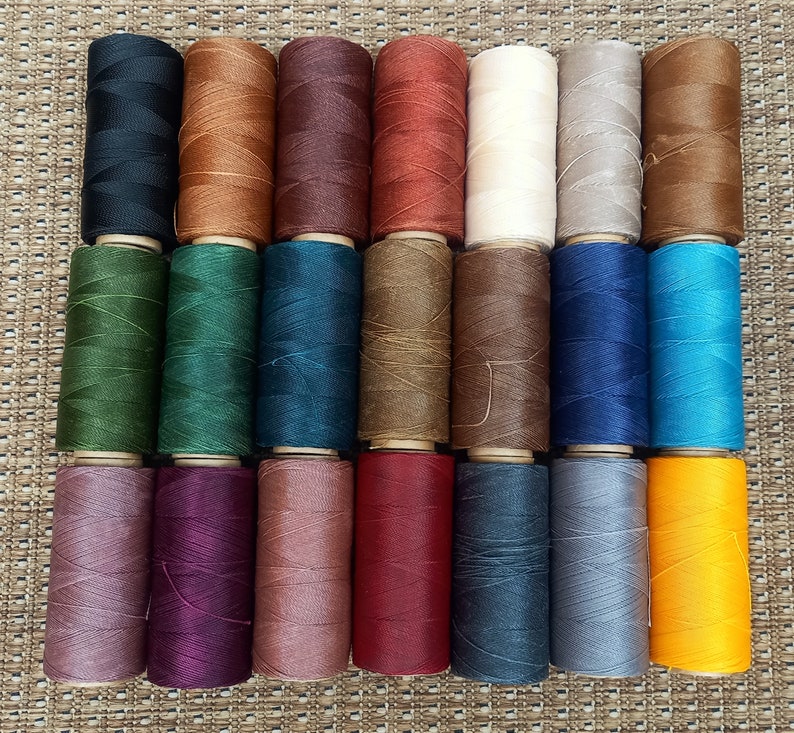 May include: A collection of 24 spools of thread in various colors, including black, brown, red, green, blue, and yellow. The spools are arranged in two rows of 12.
