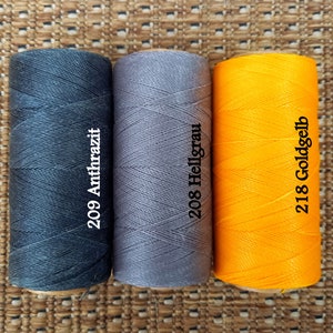 May include: Three spools of thread in different colors: black, gray, and yellow. The spools are labeled with numbers and color names: 209 Anthrazit, 208 Hellgrau, and 218 Goldgelb.