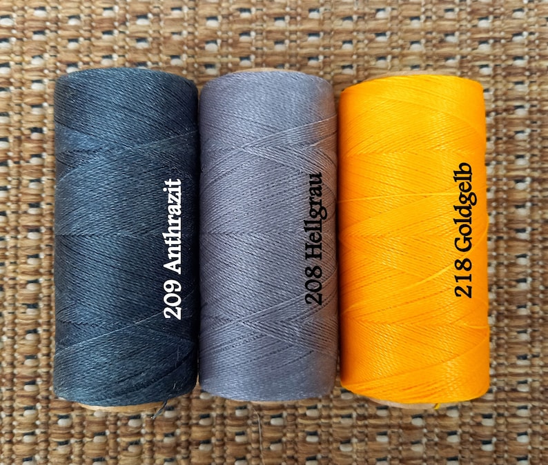 May include: Three spools of thread in different colors: black, gray, and yellow. The spools are labeled with numbers and color names: 209 Anthrazit, 208 Hellgrau, and 218 Goldgelb.