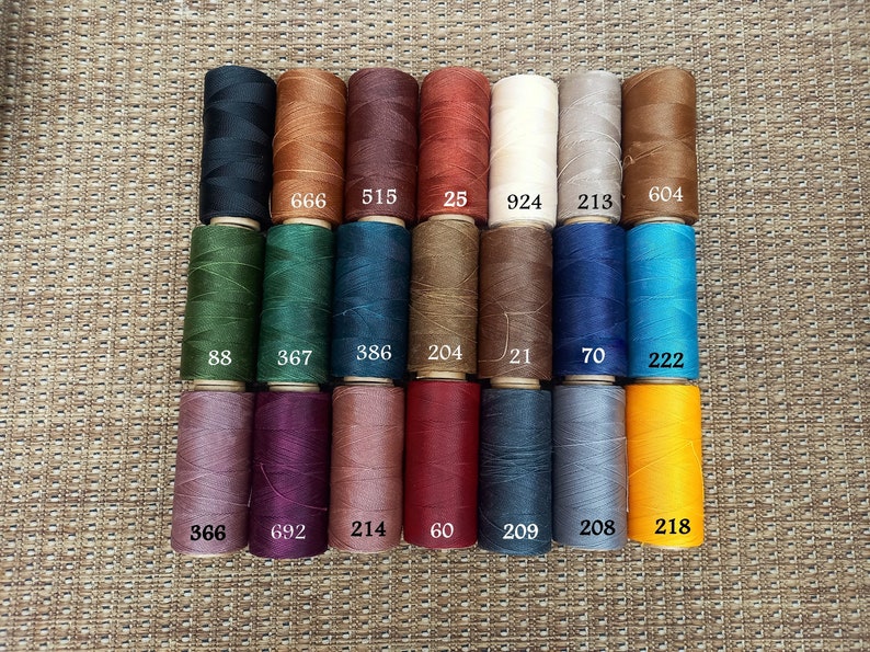May include: A collection of 18 spools of waxed thread in various colors, including black, brown, red, white, green, blue, purple, and yellow. Each spool is labeled with a number.