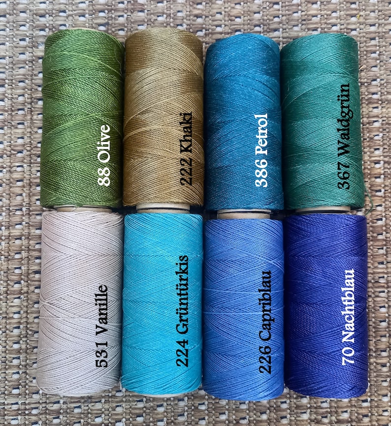 Pode incluir: Oito rolos de fio em v&aacute;rias cores, incluindo verde oliva, c&aacute;qui, azul-turquesa, azul petr&oacute;leo, bege, turquesa, azul claro e azul escuro. Cada rolo tem um n&uacute;mero e um nome de cor impresso no r&oacute;tulo.