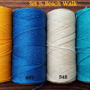 Puede incluir: Conjunto de cuatro carretes de hilo de bordar en amarillo, azul, blanco y turquesa. Los carretes est&aacute;n etiquetados con los n&uacute;meros 274, 692, 548 y 229. El texto "Set 5: Beach Walk" es visible en la parte superior de la imagen.