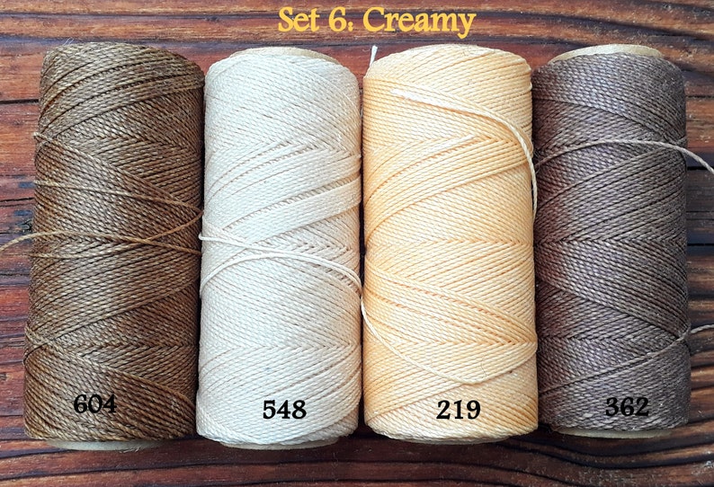 Puede incluir: Conjunto de cuatro carretes de hilo de lino encerado en tonos de marr&oacute;n, beige y crema. Los carretes est&aacute;n etiquetados con los n&uacute;meros 604, 548, 219 y 362. El texto "Set 6. Creamy" se muestra sobre los carretes.