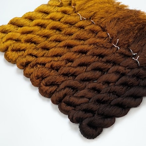 May include: A set of six skeins of ombre yarn in shades of brown and gold. The yarn is arranged in a gradient from light gold to dark brown.