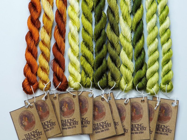 May include: A set of 10 spools of embroidery floss in shades of orange, yellow, and green. The floss is labeled "THUONG EMBROIDERY" and has a silk sheen.