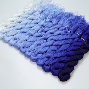 May include: A collection of blue and white embroidery floss spools arranged in a gradient from white to dark blue.