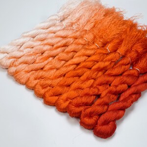 May include: A collection of ombre silk threads in shades of orange and white. The threads are twisted together and arranged in a gradient pattern, starting with white and transitioning to a deep orange.