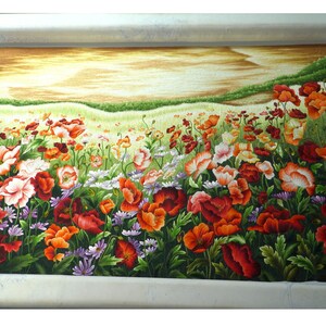 May include: A close-up of a needlepoint embroidery depicting a field of red, orange, and white poppies with green leaves and stems. The background is a soft yellow and brown, suggesting a sunset or sunrise.