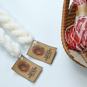 May include: Two spools of white cotton embroidery floss with brown paper tags that read "THUONG EMBROIDERY Cotton 100%". A wicker basket holds several spools of red and white embroidery floss.