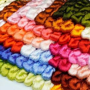 Puede incluir: Una colección de carretes de hilo de bordar de colores dispuestos en filas. El hilo es de varios colores, incluyendo rojo, naranja, amarillo, verde, azul, morado y blanco.