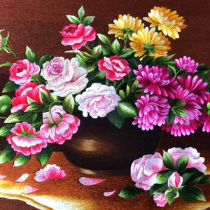 May include: A brown ceramic vase filled with a variety of pink, white, and yellow flowers. The flowers are arranged in a symmetrical pattern and are surrounded by green leaves. The vase is sitting on a brown table with a few flower petals scattered around it.