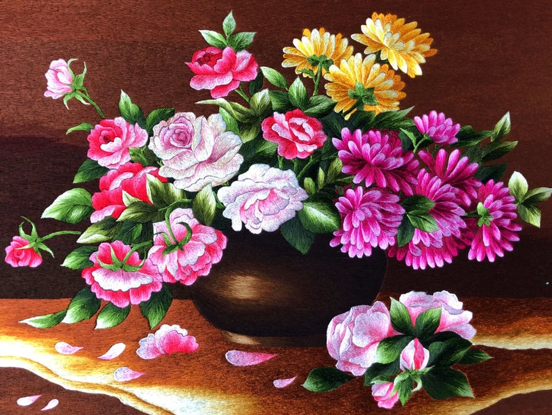 May include: A brown ceramic vase filled with a variety of pink, white, and yellow flowers. The flowers are arranged in a symmetrical pattern and are surrounded by green leaves. The vase is sitting on a brown table with a few flower petals scattered around it.