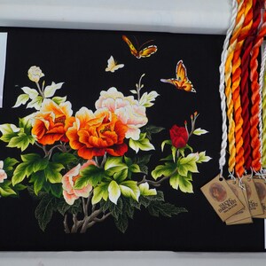 May include: Embroidered artwork featuring a floral design with red, orange, and white peonies, green leaves, and butterflies on a black background. The artwork is framed and includes a set of embroidery floss.
