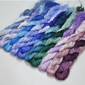 May include: A collection of 10 skeins of hand-dyed silk thread in shades of blue, green, purple, and pink. The skeins are arranged in a rainbow pattern.