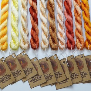 May include: Ten spools of embroidery floss in shades of yellow, orange, and red. Each spool has a brown paper tag with the text "THUONG EMBROIDERY Shiny Silk" and a corresponding number.