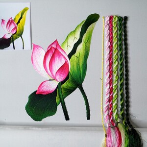 May include: Embroidered lotus flower with green leaves and a pink blossom. The embroidery is done on white fabric and the floss is in shades of pink, green, and yellow.