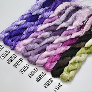 May include: A collection of 10 spools of embroidery floss in shades of purple, pink, green, and brown. The spools are labeled with the numbers ST99 through ST108.